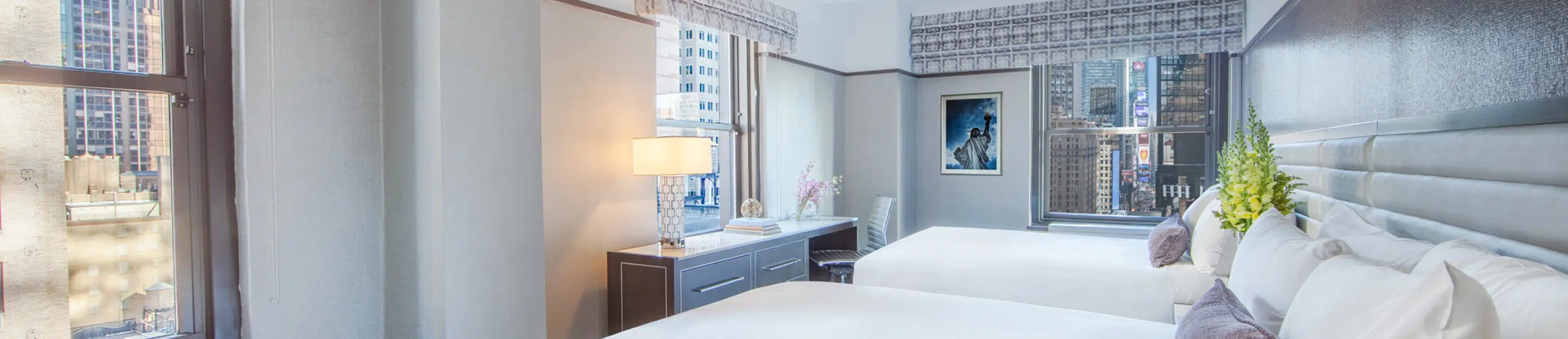 A wide view of a hotel room with two beds, a desk, and a city view.