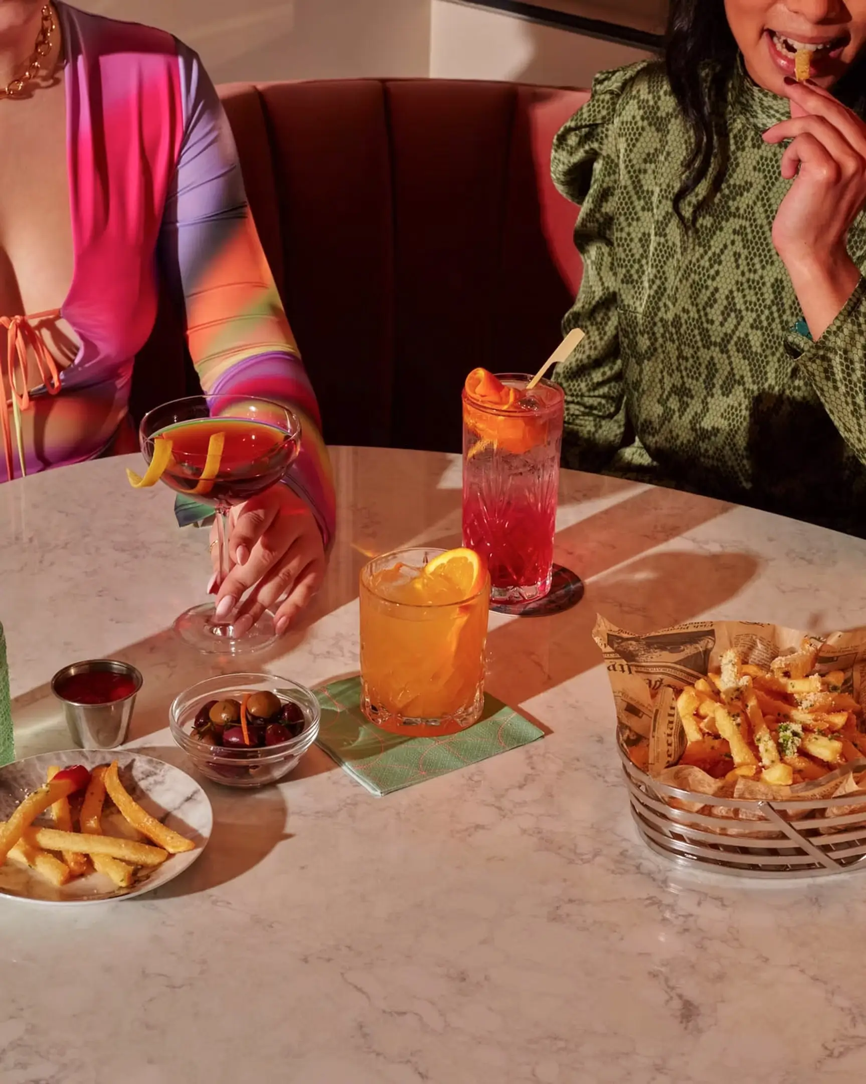 Two women sitting at a bar with drinks and snacks