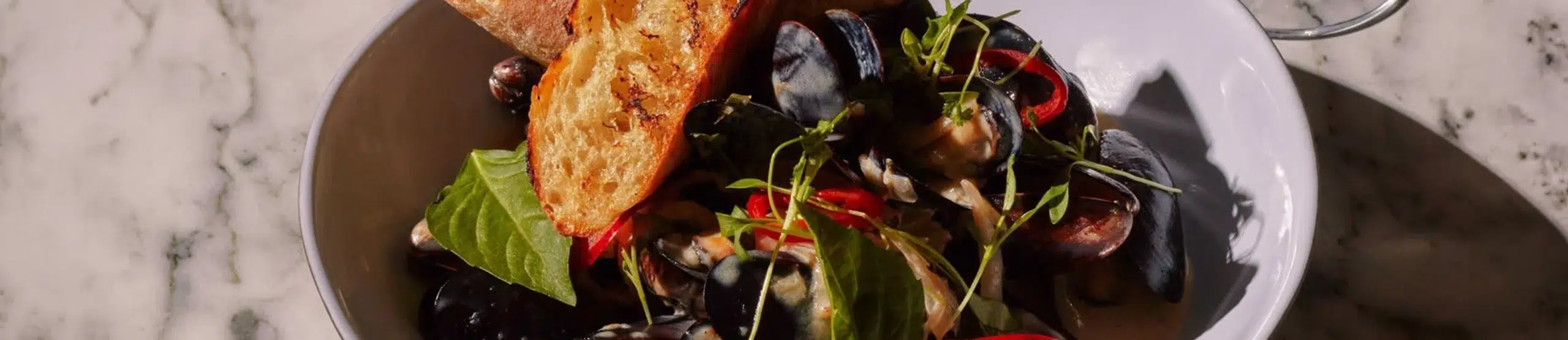 a bowl of mussels with bread and herbs