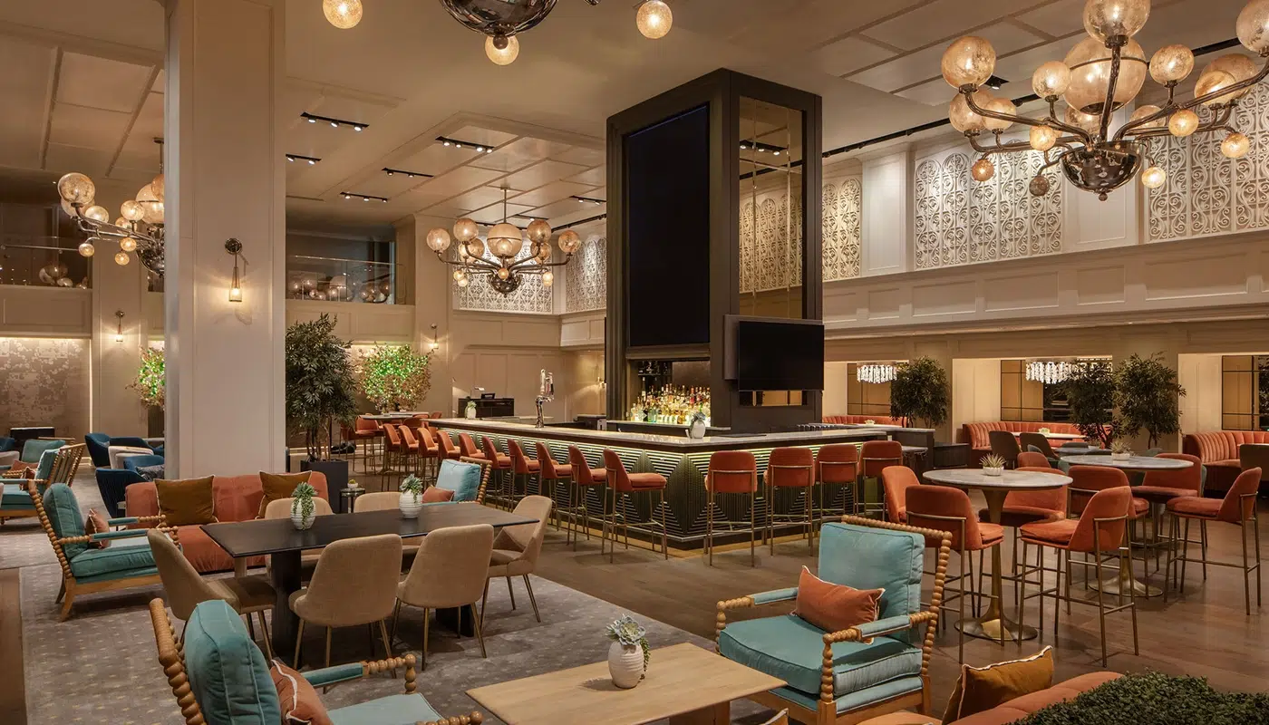 A spacious hotel lobby with a high ceiling, chandeliers, a bar, and seating areas.
