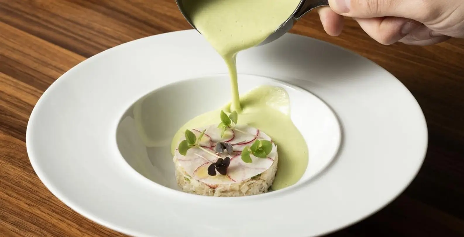 A dish being plated with a creamy sauce