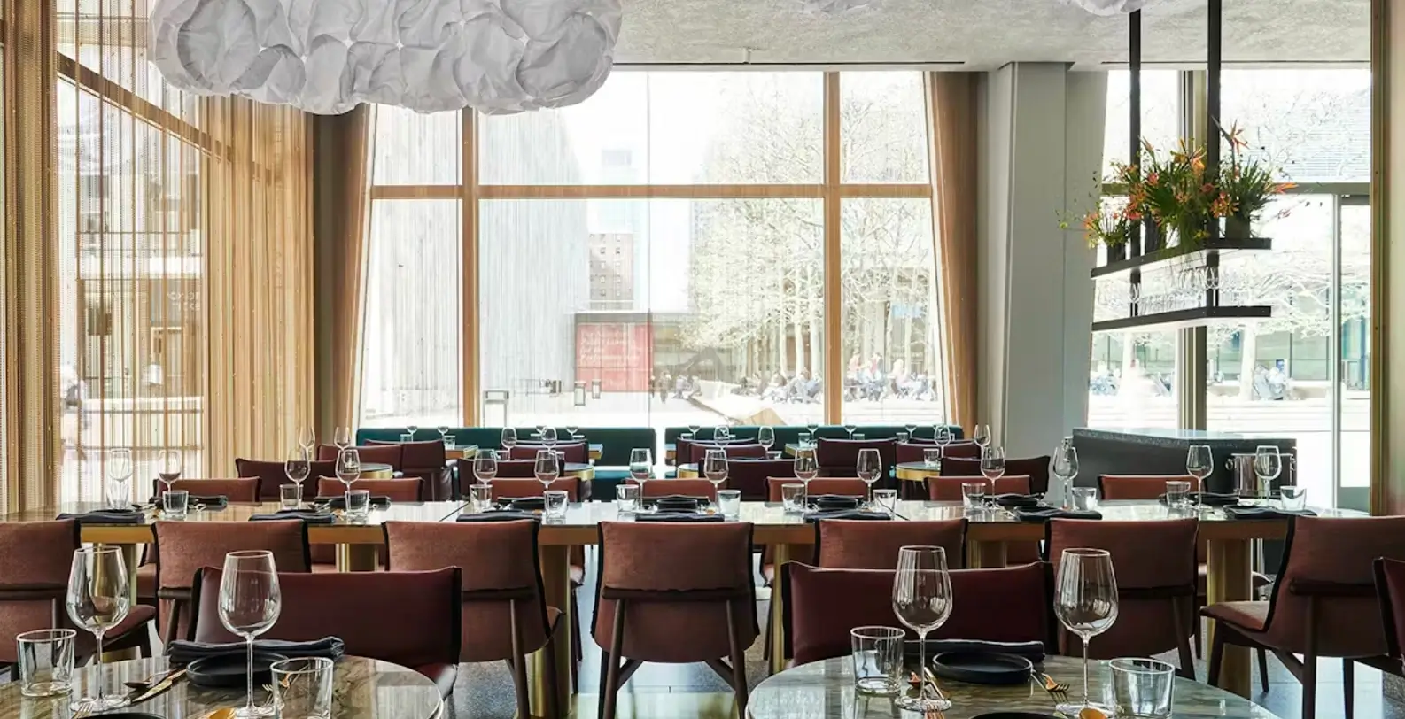 A brightly lit dining area with round tables set for meals, large windows, and modern decor.