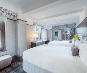 A wide view of a hotel room with two queen beds, a window, and a desk area.